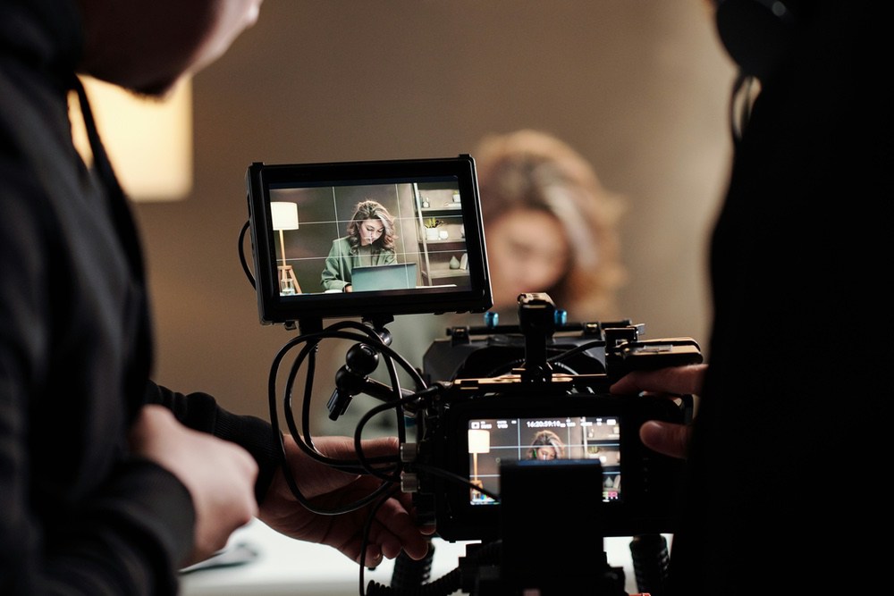 Camera operator filming a subject, framing visible on the external monitor