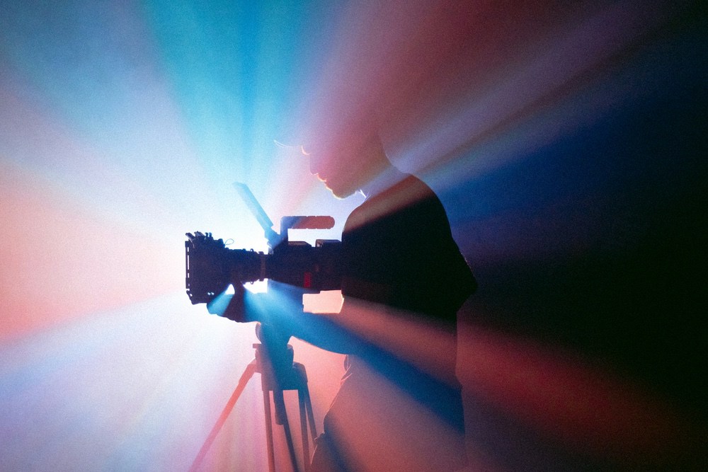 Silhouetted operator with a cinema camera and bursting light rays
